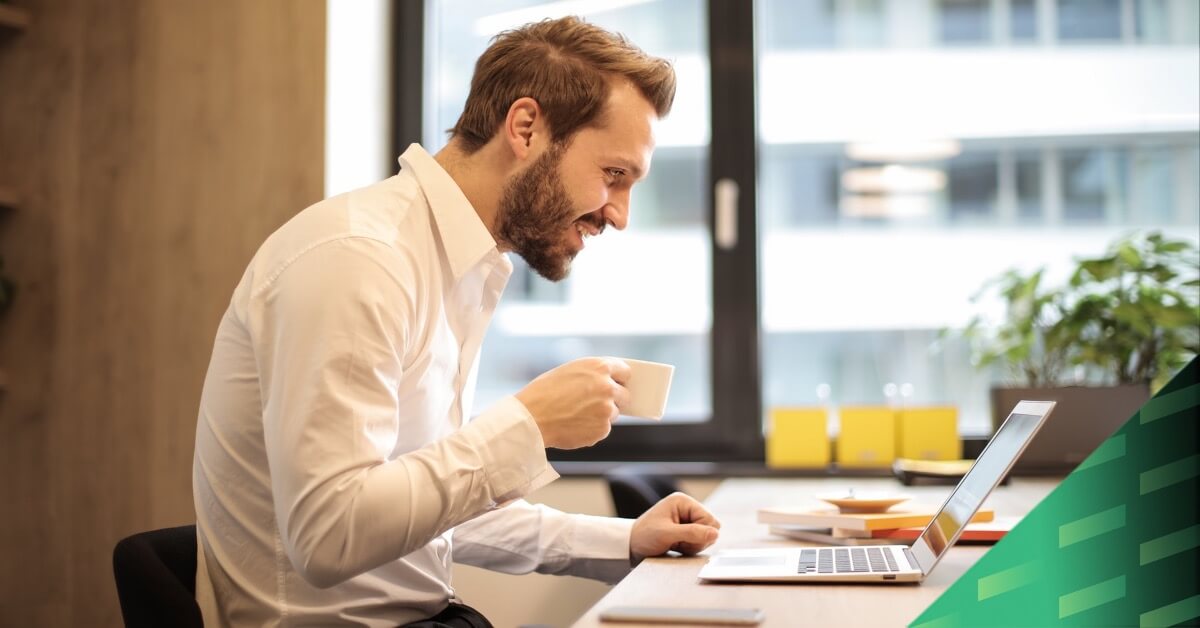 man holding teacup in front of laptop on top of table