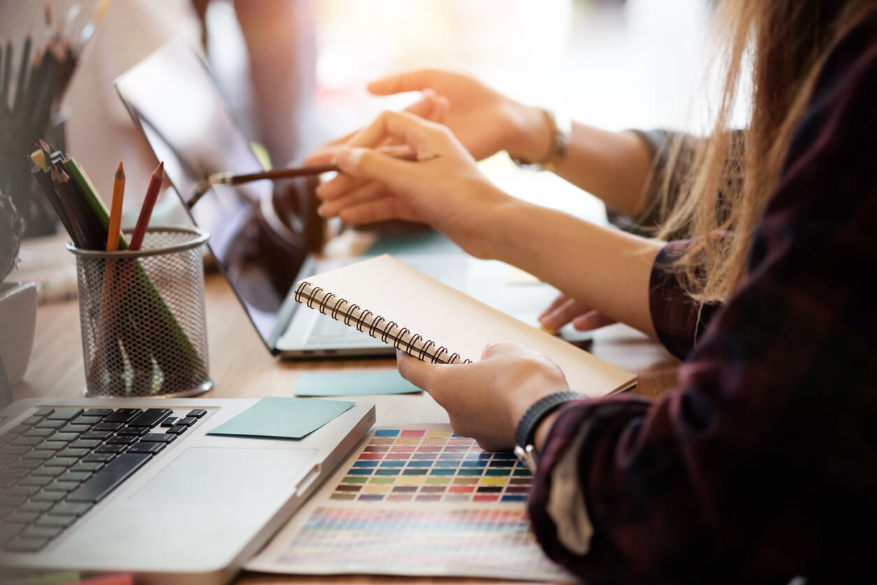 woman hand holding notebook and pointing to laptop with pencil