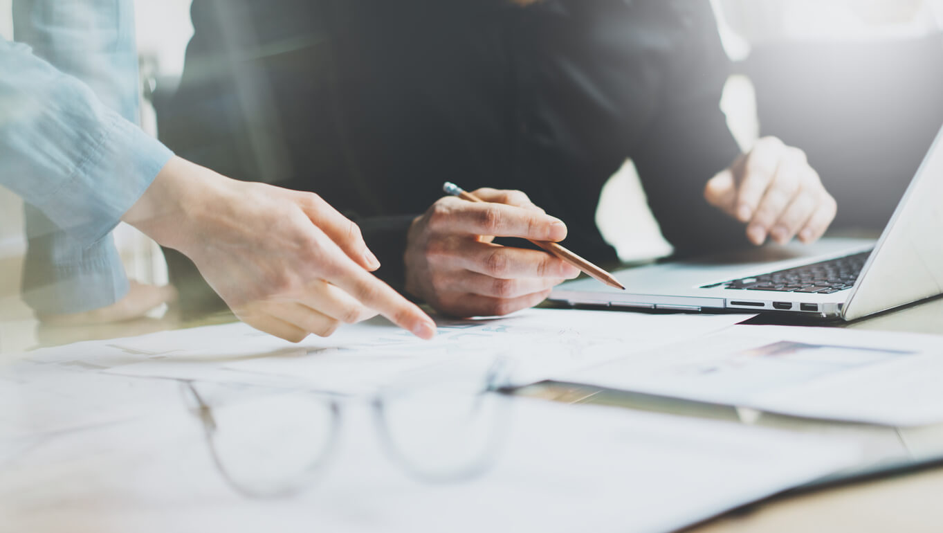 hands pointing to papers on table with laptop