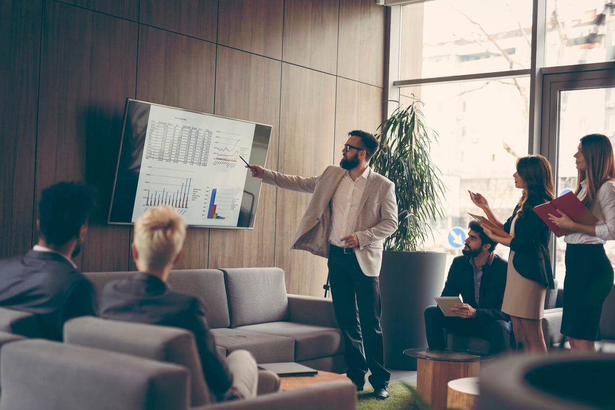 man pointing to screen on wall surrounded by people