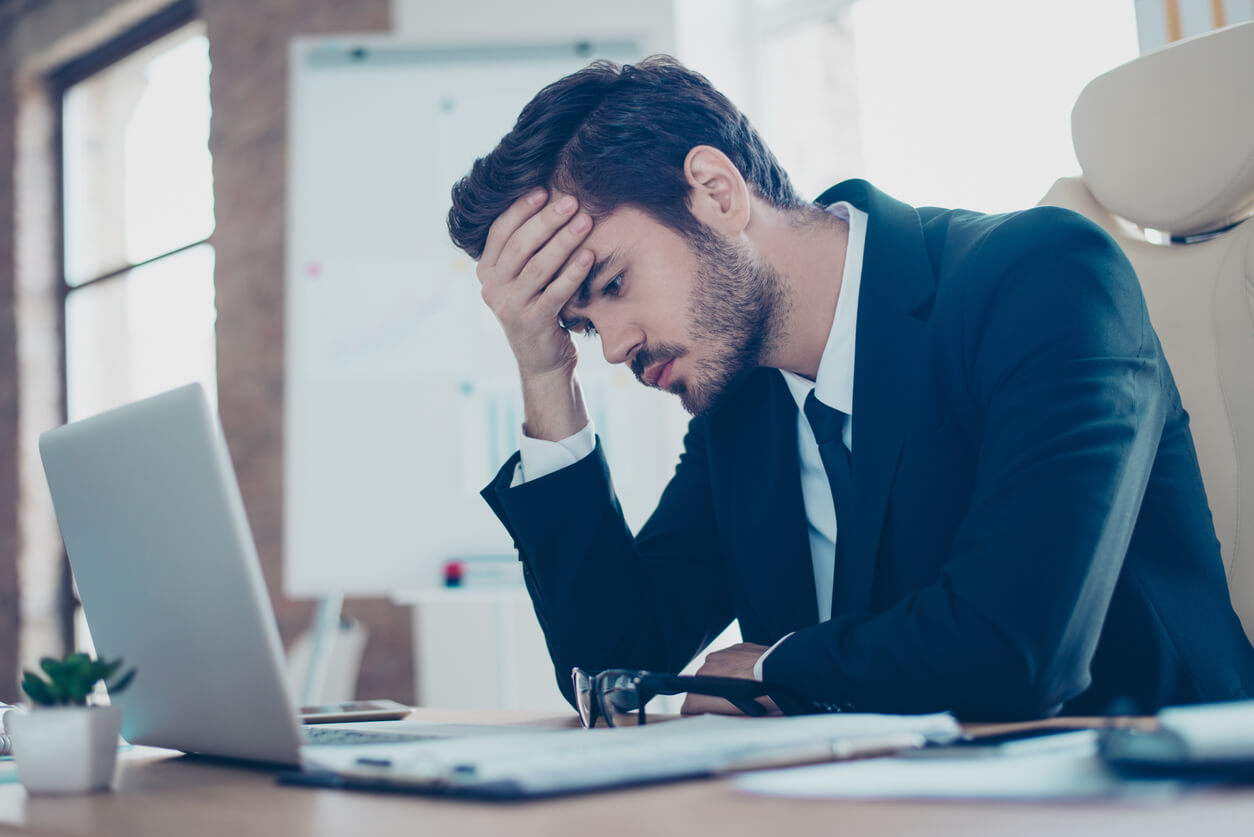 stressed man with hand on forehead in front of laptop