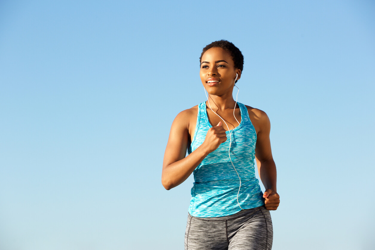 woman running with headphones in front of blue sky