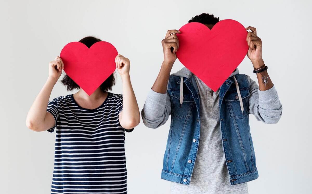 two people holding red hearts in front of faces