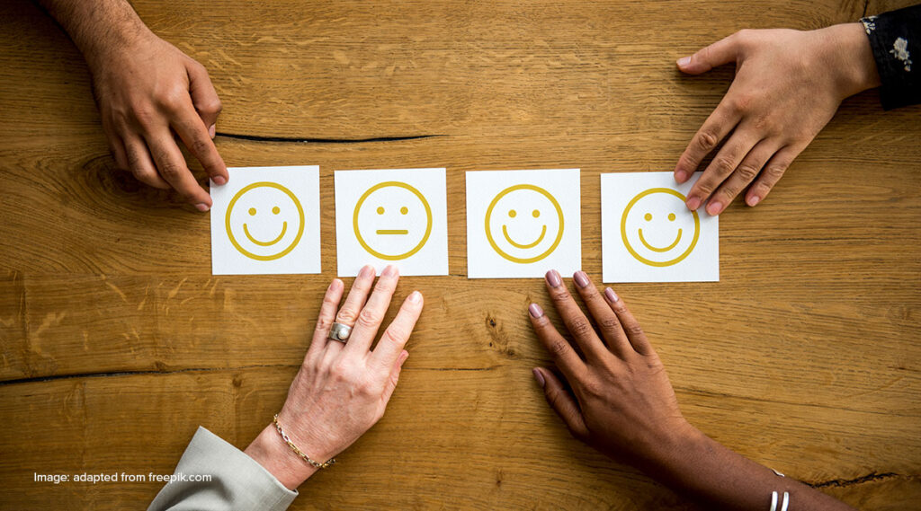 on a table, four hands place a card with a smiley on it, expressing feedback