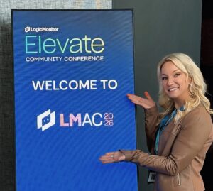 Christy Punch, Principal Analyst at Forrester, standing next to a LogicMonitor digital sign.